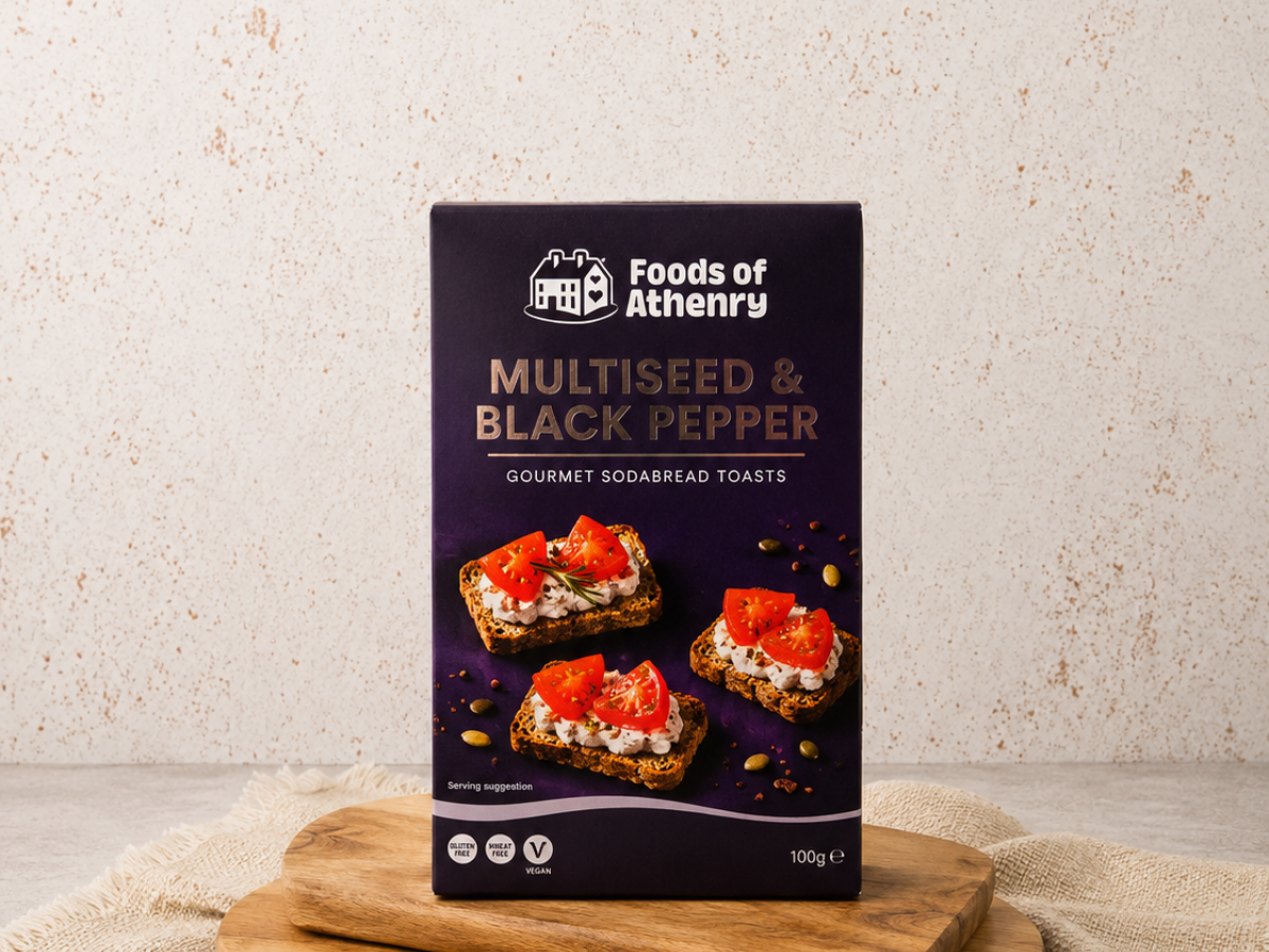 A box of Foods of Athenry Multiseed & Black Pepper Gourmet Sodabread Toasts, standing upright on a wooden tabletop against a neutral light gray background.